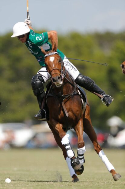 A polo player in green riding a horse playing horse polo on the field