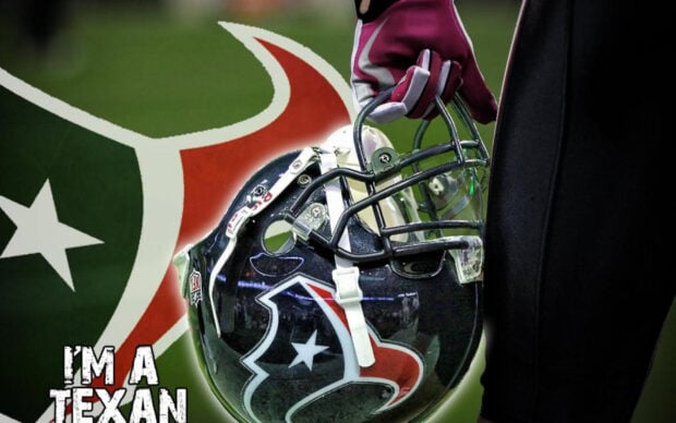 A close up of a Houston Texans helmet held by a player with a large Texans logo in the background