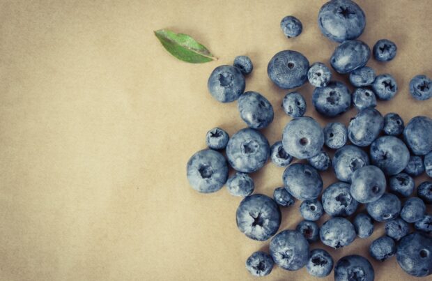 Fresh huckleberry fruits scattered on a brown surface with one green leaf visible