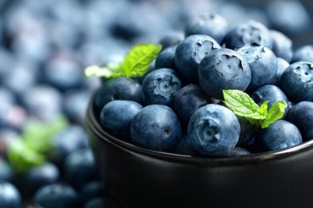 Close up of fresh huckleberry fruit in a black bowl with green leaves