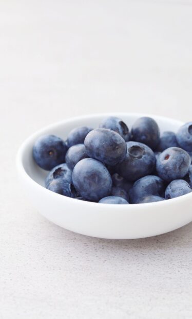 Fresh huckleberry fruits in a white bowl on a light surface