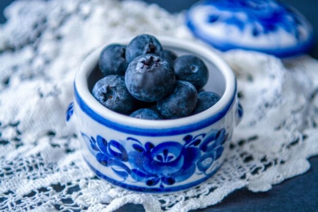 A close up view of fresh huckleberry berries in a decorated ceramic bowl on a lace tablecloth