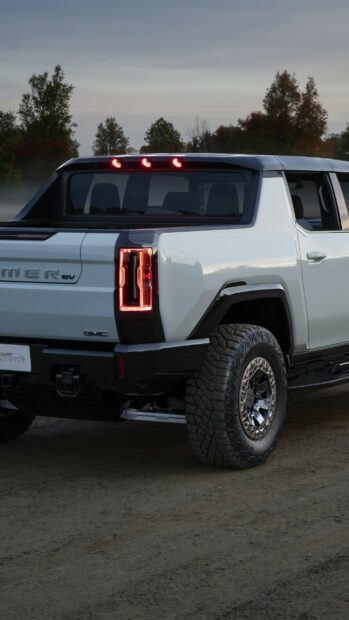 Rear side of a modern Hummer truck with illuminated taillights on a dirt road at dusk