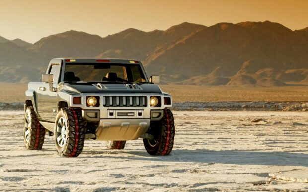 Hummer vehicle standing on a dry desert landscape at sunset with mountain background