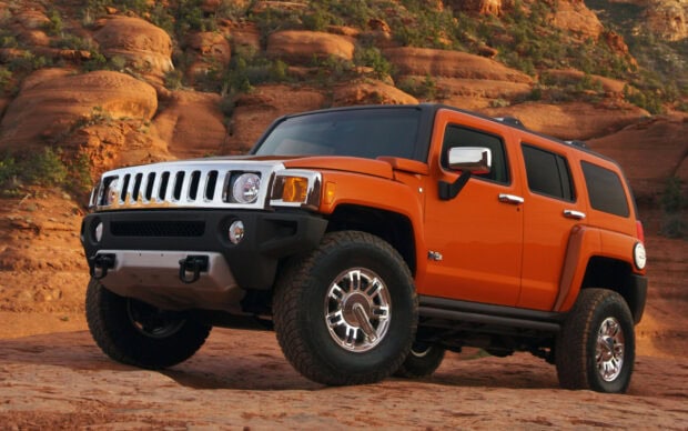 Orange Hummer driving through rocky desert terrain with rugged landscape in background
