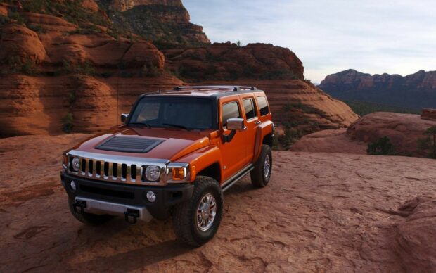 Orange hummer parked on rocky desert terrain with red cliffs in the background
