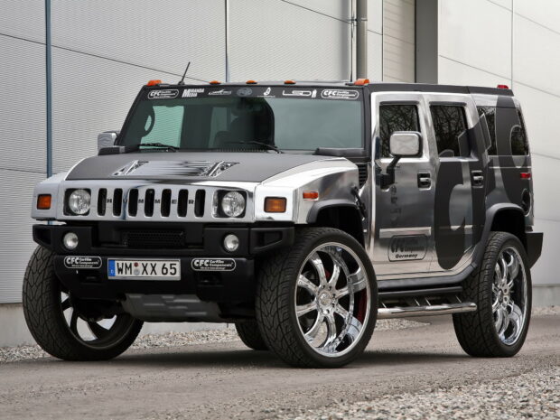 Silver Hummer vehicle with large chrome wheels parked on gravel outside a modern building