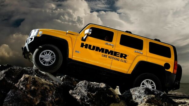 Yellow Hummer vehicle climbing rocky terrain under dramatic cloudy sky