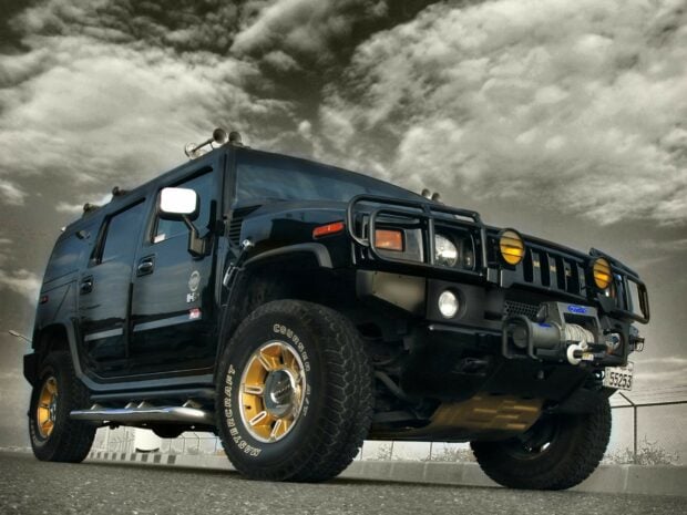 Black Hummer car with golden rims parked under cloudy sky