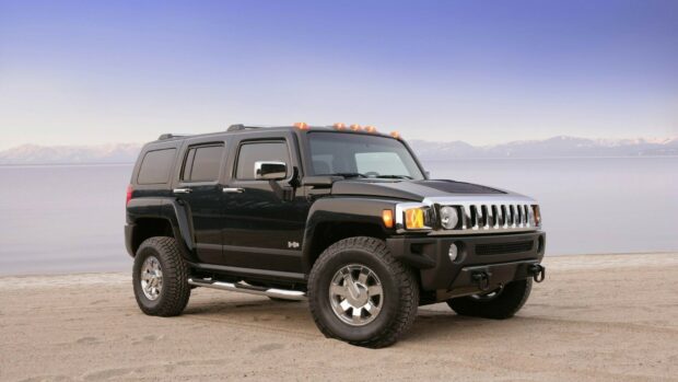 Black Hummer SUV on a sandy beach with mountains in the background