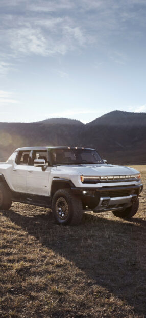 White Hummer truck parked in a grassy field with mountains in the background