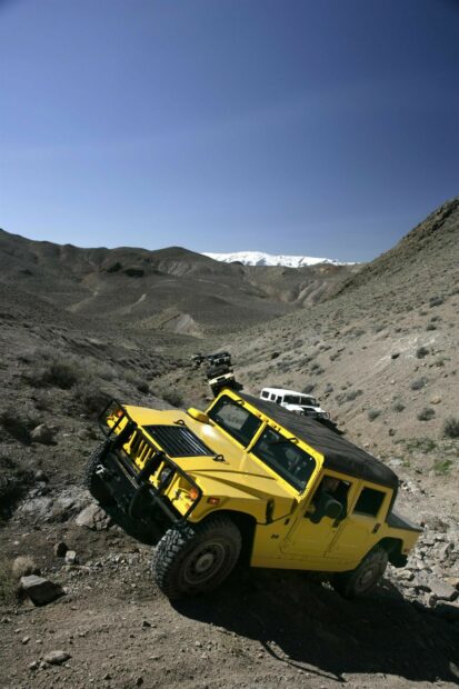 Yellow Hummer driving off road in rocky desert terrain