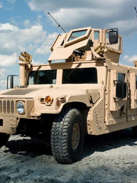 Beige military vehicle on rough terrain under blue sky with clouds