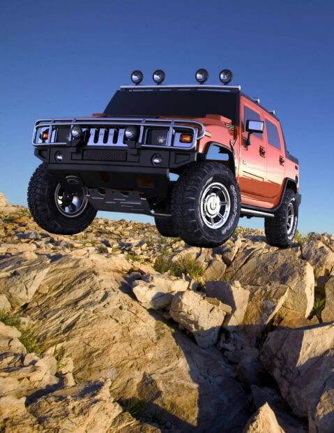 Orange Hummer truck climbing rocky terrain under clear blue sky