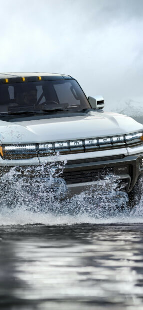 White Hummer driving through water with splashes against cloudy sky