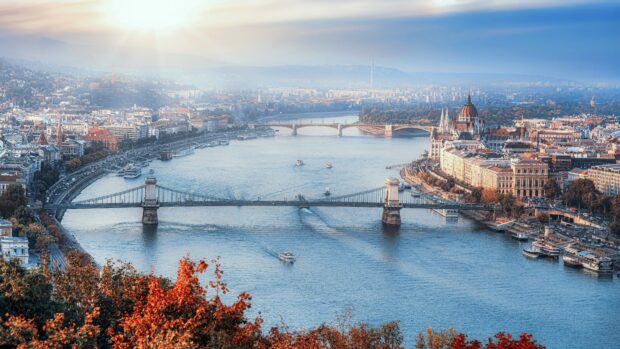 Historic bridge over the river in Hungary with cityscape and autumn trees in the foreground