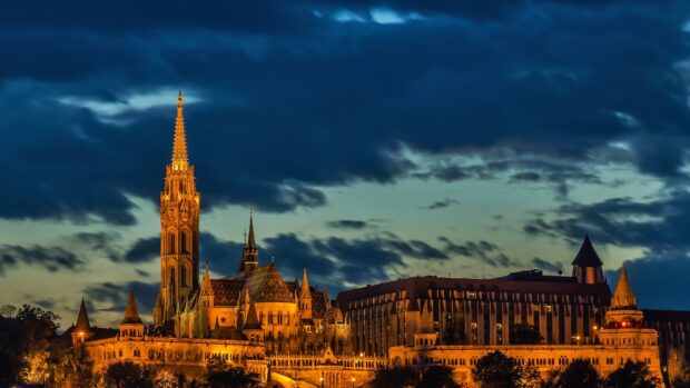 The illuminated Budapest castle complex stands against a dramatic sky at dusk in Hungary