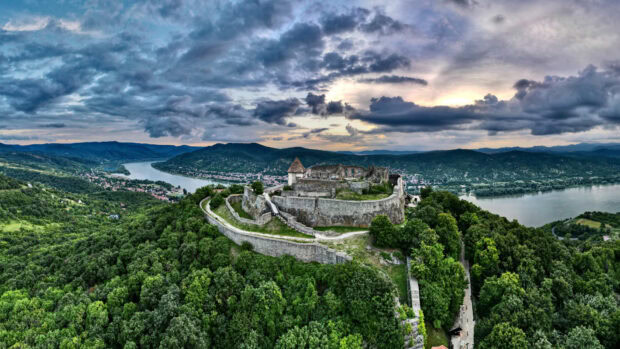 Ancient fortress in Hungary surrounded by lush greenery and a winding river under cloudy sky