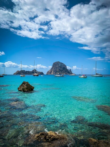 Clear turquoise water with rocks and sailboats near Ibiza islands