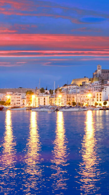 Evening view of Ibiza city with boats and colorful sky reflecting on the water