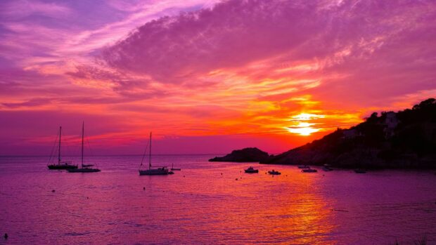 Colorful Ibiza sunset with boats sailing on calm sea waters