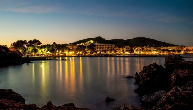 Evening view of Ibiza coastline with illuminated buildings and calm sea reflecting lights