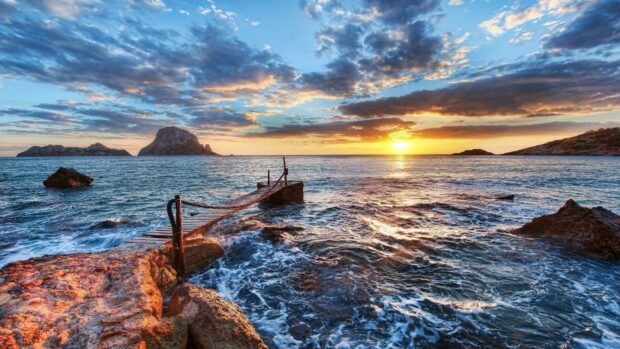 Scenic Ibiza sunset over rocky coast and wooden pier