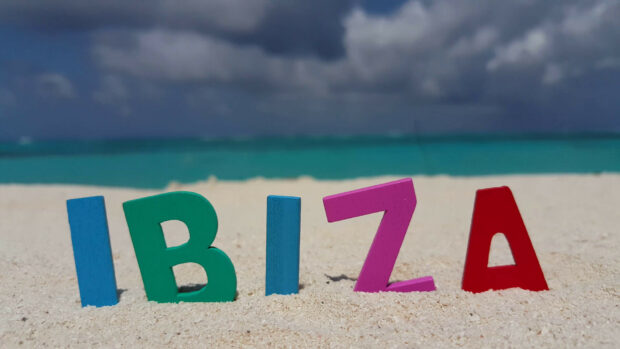 Colorful letters spelling Ibiza on sandy beach with ocean in background