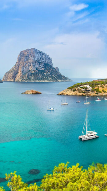 A scenic view of Ibiza coast with turquoise waters and sailing boats in a beautiful clear sky