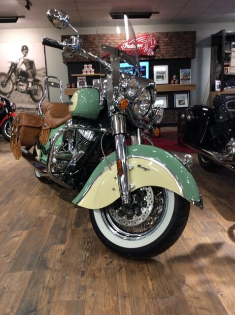 A classic Indian vintage motorcycle with leather saddlebags displayed indoors on wooden flooring