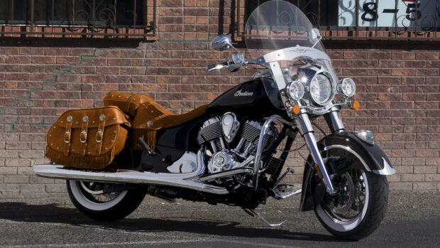 A vintage Indian motorcycle with leather saddlebags parked against a brick wall