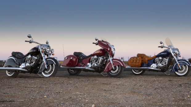 Three Indian vintage motorcycles parked on rocky ground under a clear sky