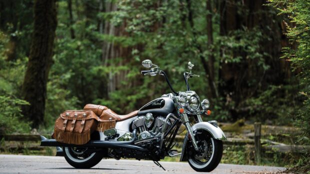 Vintage Indian motorcycle with leather saddlebags parked on forest road with green trees in background