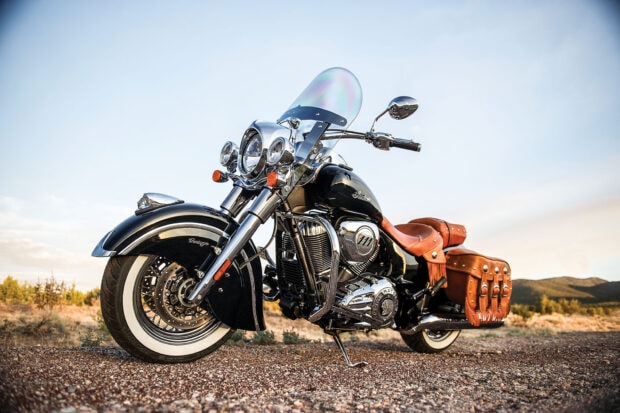 A classic Indian vintage motorcycle with leather saddlebags parked on a gravel road at sunset