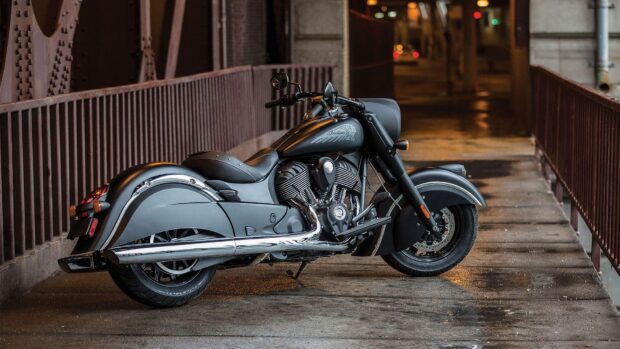 Black Indian vintage motorcycle parked on a rainy street under a bridge at night