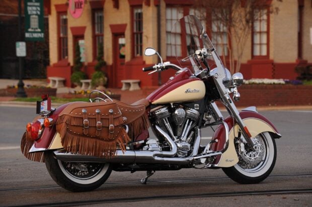A classic Indian vintage motorcycle with leather fringe saddlebags parked on a street in front of a historic building