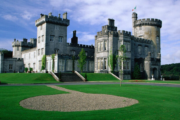 A historic Irish castle with stone towers and manicured green lawn under a blue sky