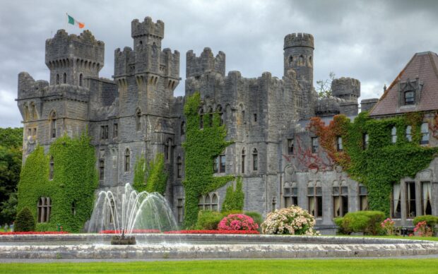 Ancient Irish castle covered with ivy and surrounded by a water fountain and blooming flowers