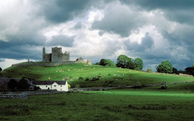 Ancient Irish castle on green hill under cloudy sky in countryside