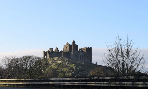 Ancient Irish castle standing on a rocky hill surrounded by trees and clear blue sky