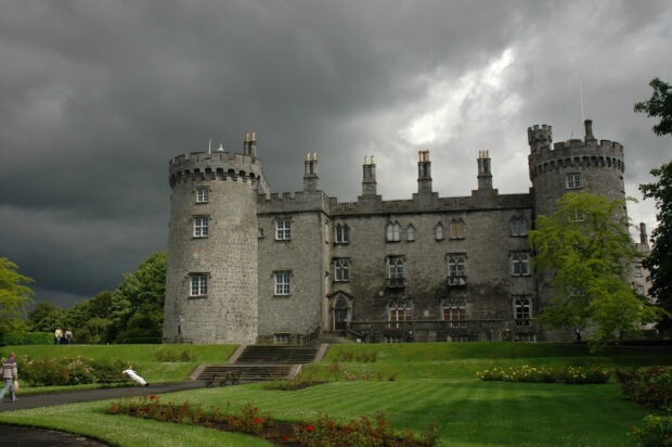 Historic castle with stone towers and green lawn under dramatic cloudy sky