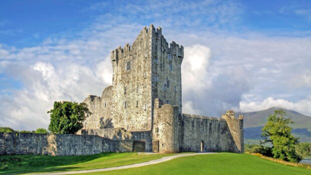 Ancient stone castle with green grass and cloudy sky in Ireland