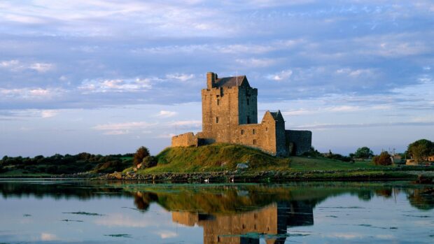 Ancient Irish castle on green hill reflecting in calm water during sunset