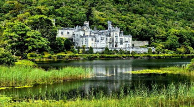 A historic Irish castle surrounded by lush greenery and reflected in a calm lake