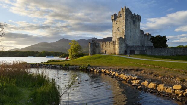 Historic Irish castle near a lake with swans and mountain views at sunset