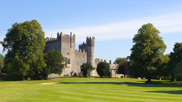 Historic Irish castle surrounded by lush green trees and a manicured lawn in clear daylight