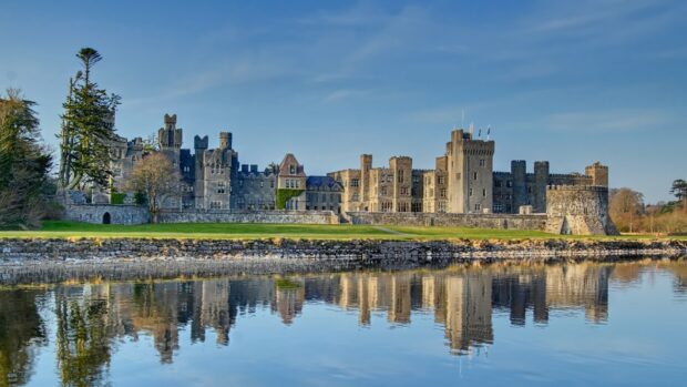 A historic Irish castle with stone walls reflected in calm water under a blue sky