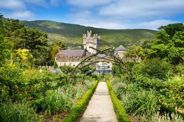 A serene castle garden path leading to an ancient Irish castle surrounded by lush greenery and hills