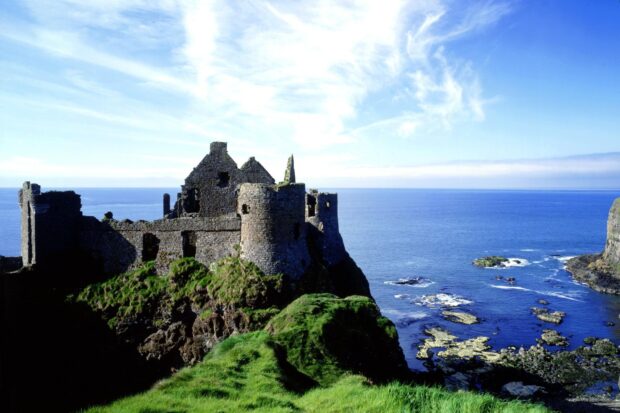 Ancient Irish castle ruins on green cliffs by the blue ocean under a bright sky