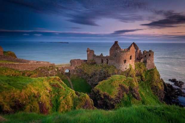 Ancient Irish castle ruins on green cliffs overlooking the ocean at sunset